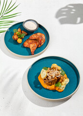 Composition from main courses in ceramic dishes: roasted chicken and beef. Set of meat dishes on white concrete background with shadows and palm leaves. Summer food menu. Modern concept. Still life.
