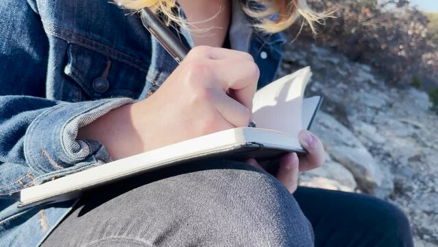 close up of person writing in journal outside in nature