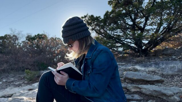 sun flare behing person as they write in book on a mountain