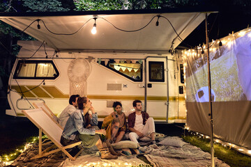 Young cheerful people watching a movie at camping site - obrazy, fototapety, plakaty