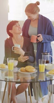 Vertical video of happy caucasian lesbian couple having breakfast at home