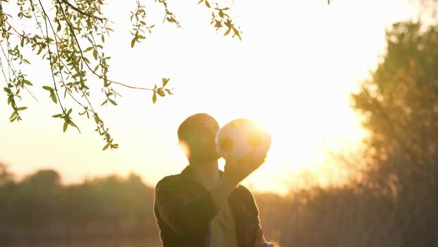 Young Man Throws Soccer Ball Up And Kicks It With His Head On Background of Sunset. 4k
