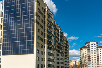 Obraz premium Movement of clouds against the background of a modern energy-efficient building. Multi-storey residential building with solar panels on the wall. Renewable energy in the city