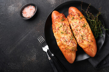 Baguette boats. Hot baked sandwich on baguette bread with ham, bacon, vegetables and cheese on parchment and black dark concrete background. Top view. Copy space.