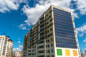 Movement of clouds against the background of a modern energy-efficient building. Multi-storey residential building with solar panels on the wall. Renewable energy in the city