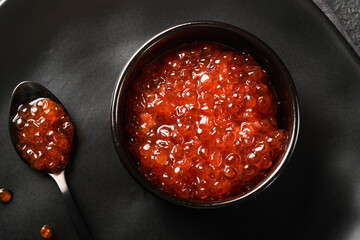 Red salmon caviar. Delicious red caviar in black bowl on black dark concrete background. Top view with copy space. Flat lay. Mock up.