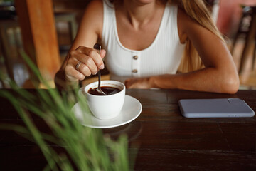Girl's hands mixing coffee in a white cup on a wooden table