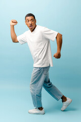 Full length studio portrait of young shocked African-American man hurrying, scared frightened...
