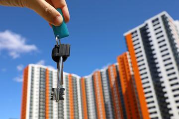 House keys in male hand on background of new residential buildings. Real estate agent, moving home...