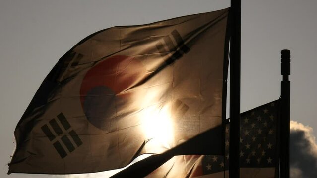 Silhouetted South Korean and UAS flags fluttering against a red sunset sky, South Korea.