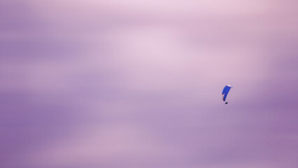 Man flying on parachute in the purple sky in sunset
