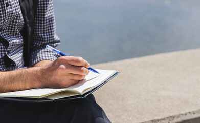 Male hand pen and diary, Man writing notes entries in diary outdoors.