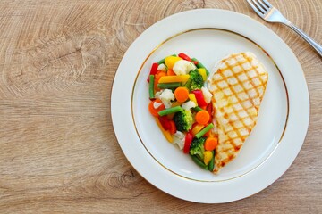 Heart shape grilled chicken breast with steamed vegetables on plate with wooden table background.Love healthy food concept for Valentine's day and Mother's day.Top view.Copy space