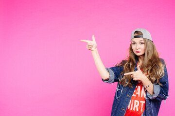 Teen girl in cap pointing at side and showing by fingers.