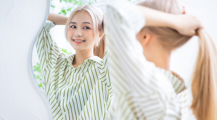 Young Asian woman tying her hair in front of a mirror