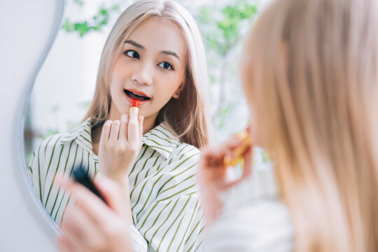 Young Asian woman applying lipstick in front of mirror