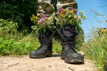 Black military boots with flowers. Concept - flowers instead of bullets and war. Ending the war in Ukraine. The surrender of the Russian army and the withdrawal of troops from the territory of Ukraine