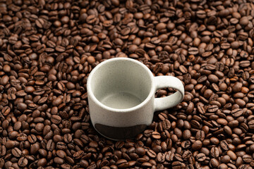 Small empty coffee cup placed onto bed of roasted coffee beans close up