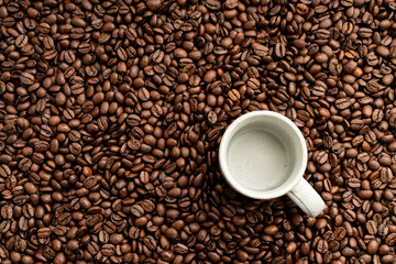 Small empty coffee cup placed onto bed of roasted coffee beans flat lay view