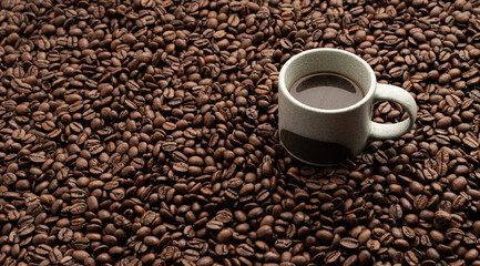 Small coffee cup filled up with hot coffee placed onto bed of roasted coffee beans