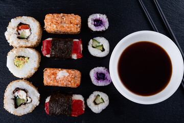 Close up of delicious japanese food with vegetarion sushi rolls  with beetroot and cucumber  with black chopsticks  and  soy sauce on black background
