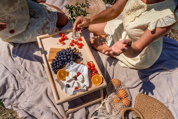 Romantic picnic for two with fruit, bread and cheese. Oranges, cherries, black grapes and camembert on a wooden table. The girl's hands with a manicure tear off a grape berry sitting on a light