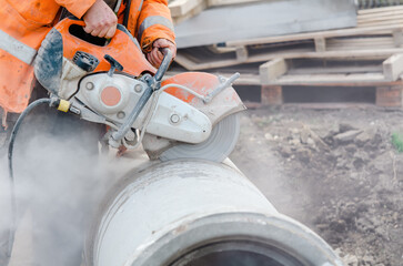 A worker at the construction site cutting a concrete drainage pipe with a petrol concrete saw....
