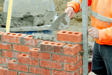 Bricklayer laying bricks on mortar on new residential house construction