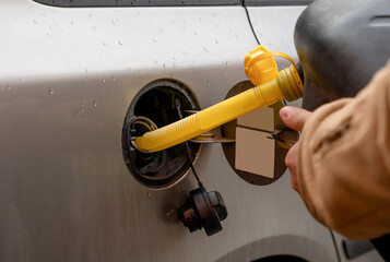 A man filling fuel tank of his car with diesel fuel off the jerry can as there is no fuel at the petrol station, close up. - obrazy, fototapety, plakaty