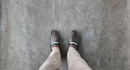 businessman in brown vintage casual shoes and beige slacks seen form above. relax standing of young businessman on grey concrete floor. fashion and footwear concept, close up of man legs. - Powered by Adobe