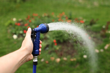 Watering green garden with outdoor hose. hand with hose sprinkle watering plants in the garden....