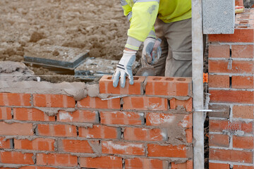 Bricklayer laying bricks on mortar on new residential house construction. Get NVQ in bricklaying