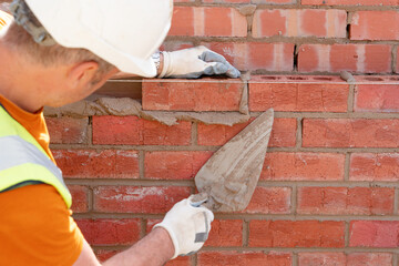 Bricklayer laying bricks on mortar on new residential house construction. Get NVQ in bricklaying - obrazy, fototapety, plakaty