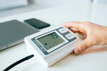 Young man checking, measuring blood pressure with digital tonometer at home holding medical electronic device.