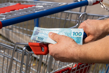 Shopping basket from a supermarket and Brazilian money held in Hands, Concept of inflation, More...