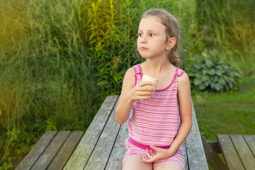 Naklejka premium a girl sits on a bench in the summer and eats ice cream