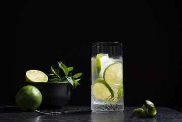 Un vaso de refrescante cóctel de jugo de lima con rodajas de lima y hielo sobre fondo negro	