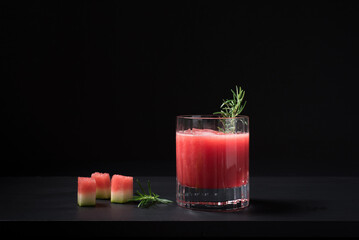 Un vaso de jugo de sandía batido con hielo servido con romero. Cóctel de frutas en fondo negro	