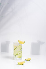 Un vaso de zumo de pepino y lima. Coctel desintoxicante con fruta y hielo sobre una mesa blanca con sombras en la pared
