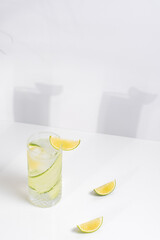 Un vaso de zumo de pepino y lima. Coctel desintoxicante con fruta y hielo sobre una mesa blanca con sombras en la pared