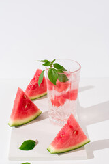 Un vaso de zumo de sandía con trozos de sandia y hielo sobre fondo claro	