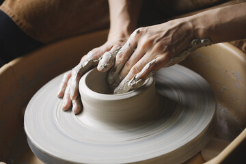 Potter's hands molding clay bowl on pottery wheel, ceramic studio workshop, close up hands and raw clay