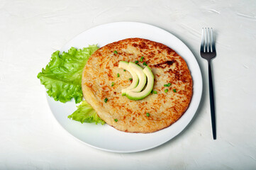 traditional Swiss dish is a potato pancake on a white plate decorated with a leaf of green lettuce and avocado, with a fork next to the plate.