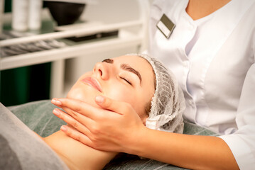 Fototapeta na wymiar Facial massage. Hands of a masseur massaging neck of a young caucasian woman in a spa salon, the concept of health massage