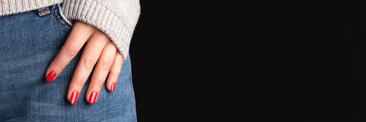 Female hand with beautiful manicure - red nails on jeans denim textile and black background with copy space banner. Wide panoramic header