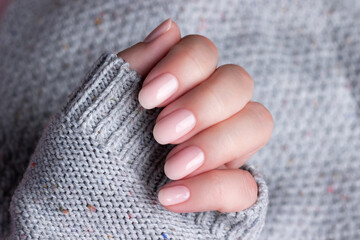 Female hand in gray knitted sweater with beautiful natural manicure - pink nude nails. Nail care...