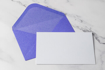 Open violet envelope with blank white post card on light marble background.