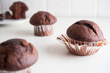 Delicious chocolate muffins in paper cups on white kitchen background. Homemade biscuit cake for breakfast