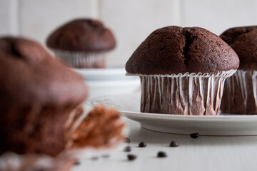 Delicious chocolate muffins in paper cups on a plate on white background.