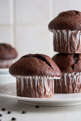 Delicious chocolate muffins in paper cups on a plate on white background.